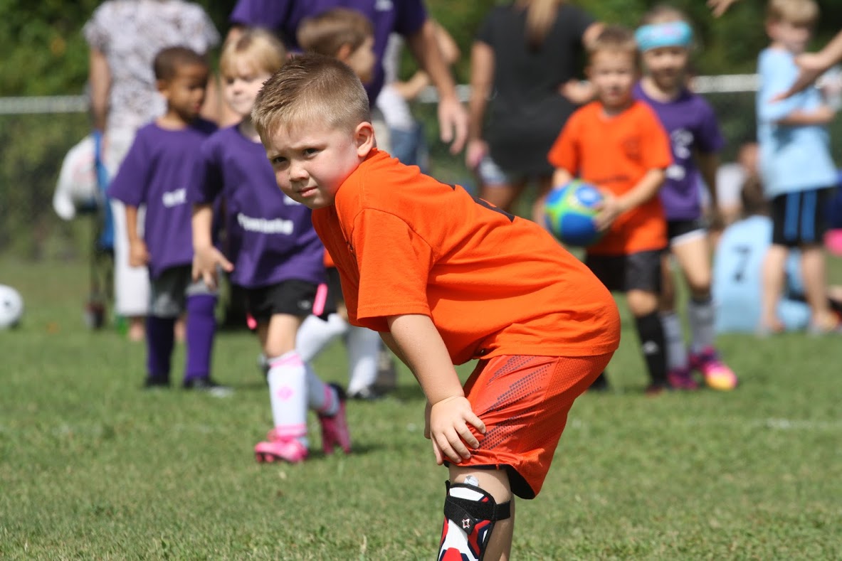 Children playing soccer; players wearing orange and purple